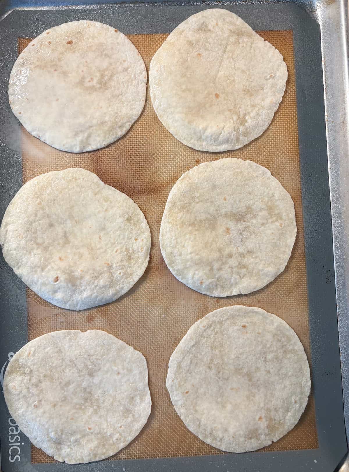 Mini tortillas on a baking sheet, sprayed with cooking spray.