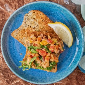 A plate with 2 slices of toast; one of them has sautéed vegetable hash on it. Garnished with a lemon slice.