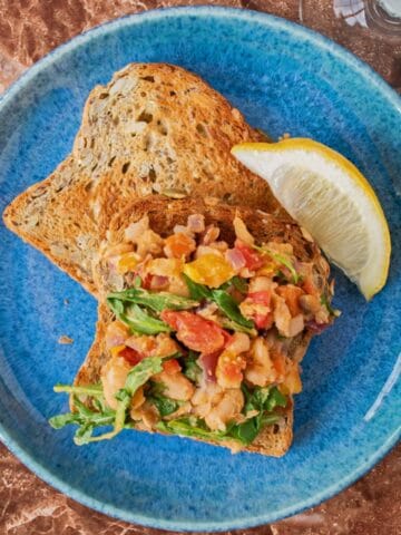 A plate with 2 slices of toast; one of them has sautéed vegetable hash on it. Garnished with a lemon slice.