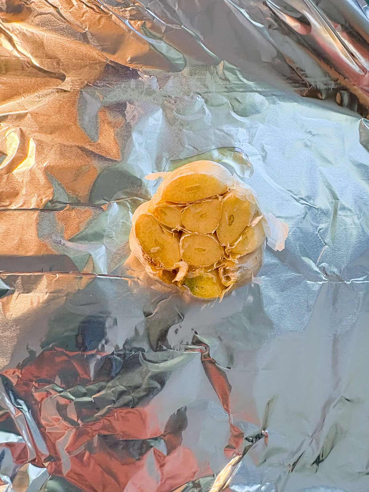 Bulb of garlic, drizzled with olive oil, on a piece of aluminum foil.