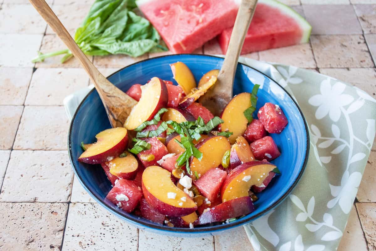 Fruit salad in a bowl with wooden serving utensils.