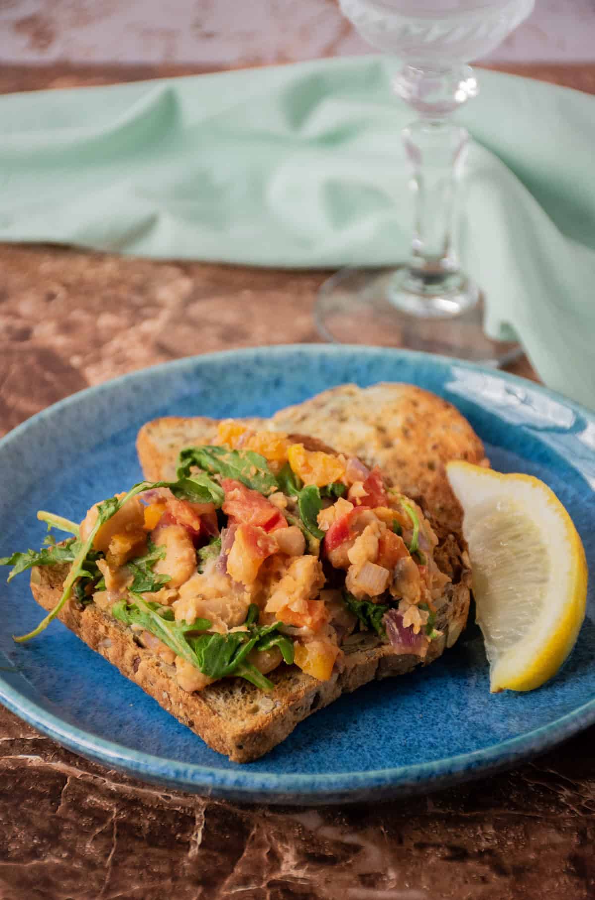 A plate with 2 slices of toast; one of them has sautéed vegetable hash on it. Garnished with a lemon slice.