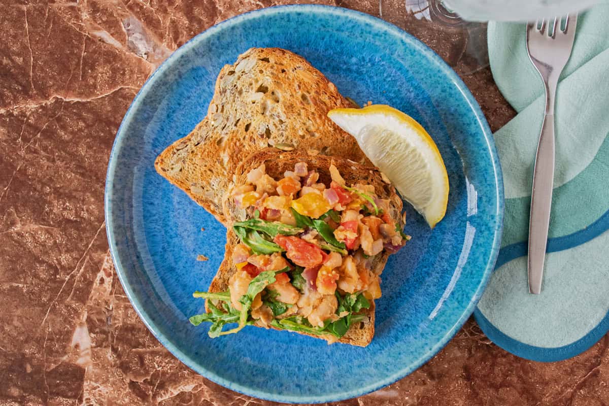 A plate with 2 slices of toast; one of them has sautéed vegetable hash on it. Garnished with a lemon slice.