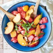 Overhead image of fruit salad with wooden serving utensils, in a blue bowl.