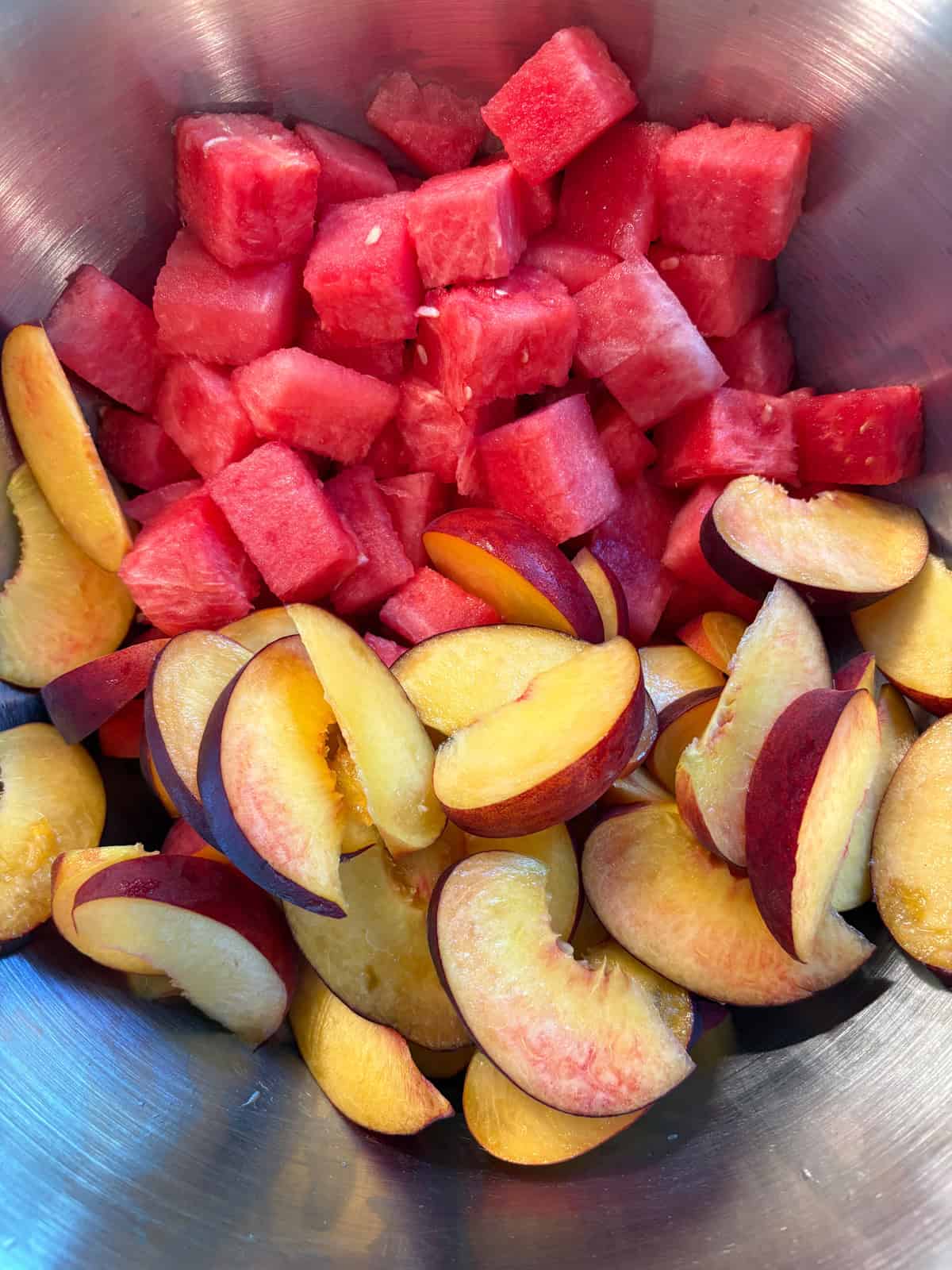 Cubed watermelon and sliced peaches together, in a mixing bowl.