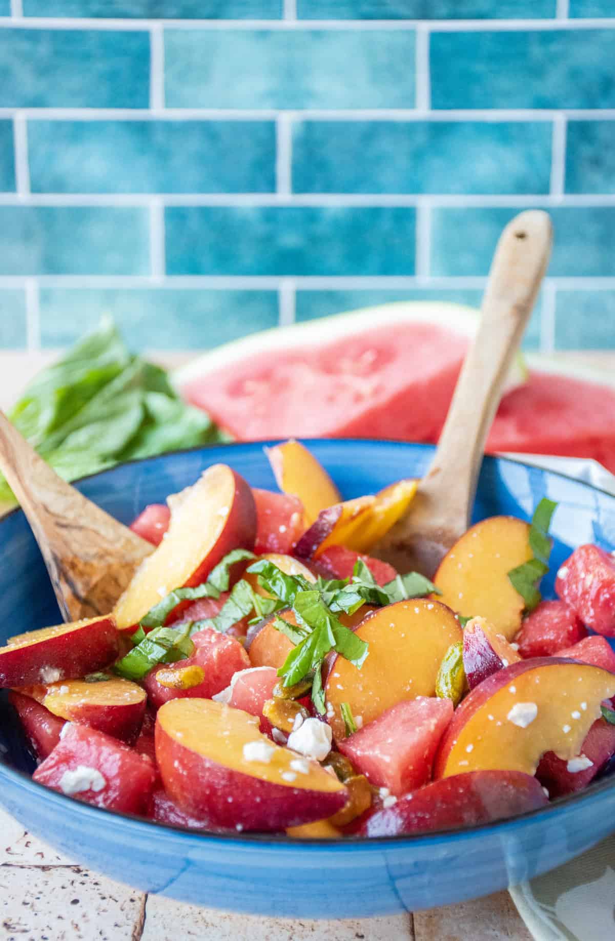 Fruit salad in a bowl with wooden serving utensils.