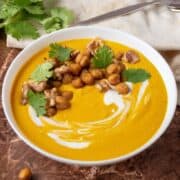 Bowl of ginger carrot soup, garnished with chickpeas, walnuts, and cilantro.