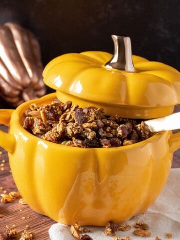 A large pumpkin shaped ramekin bowl filled with granola.