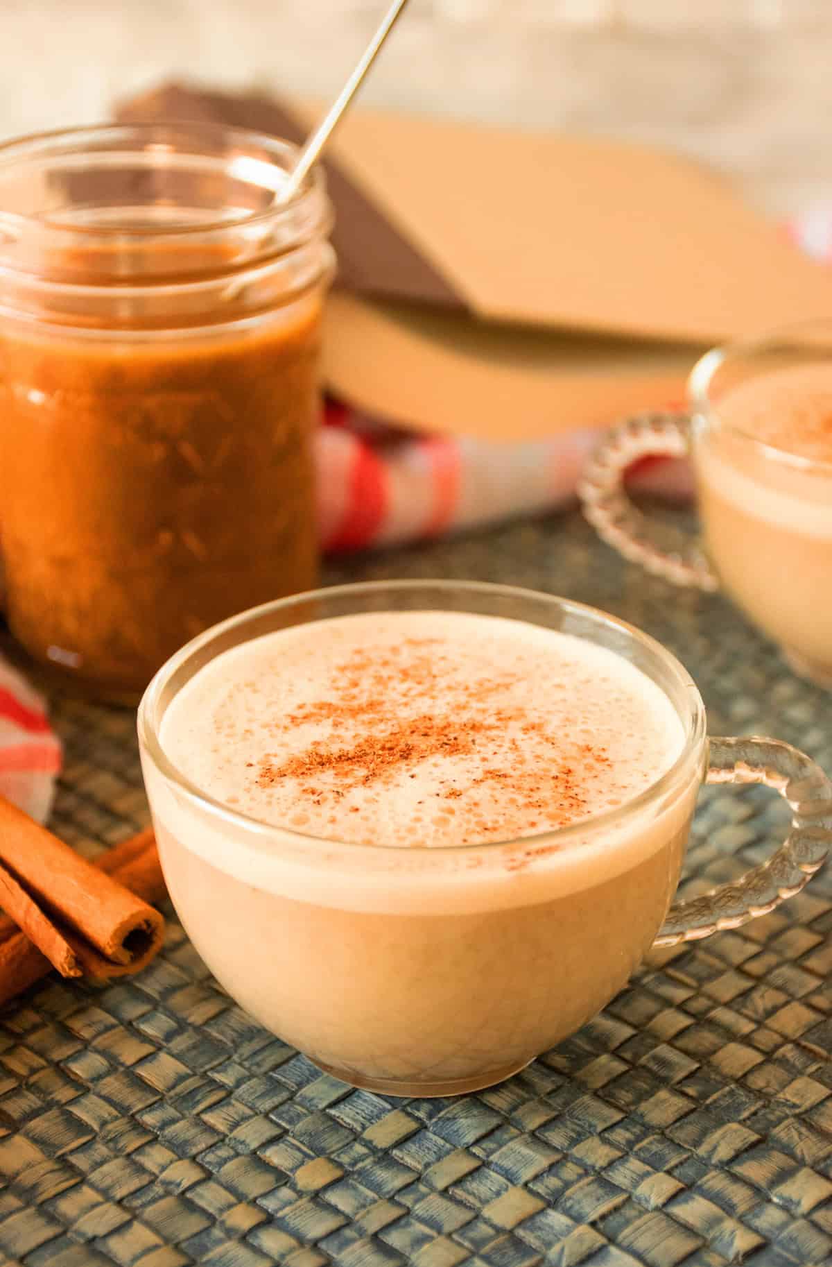 A glass mug containing a pumpkin spice latte made with healthy pumpkin spice syrup, seen in the background.