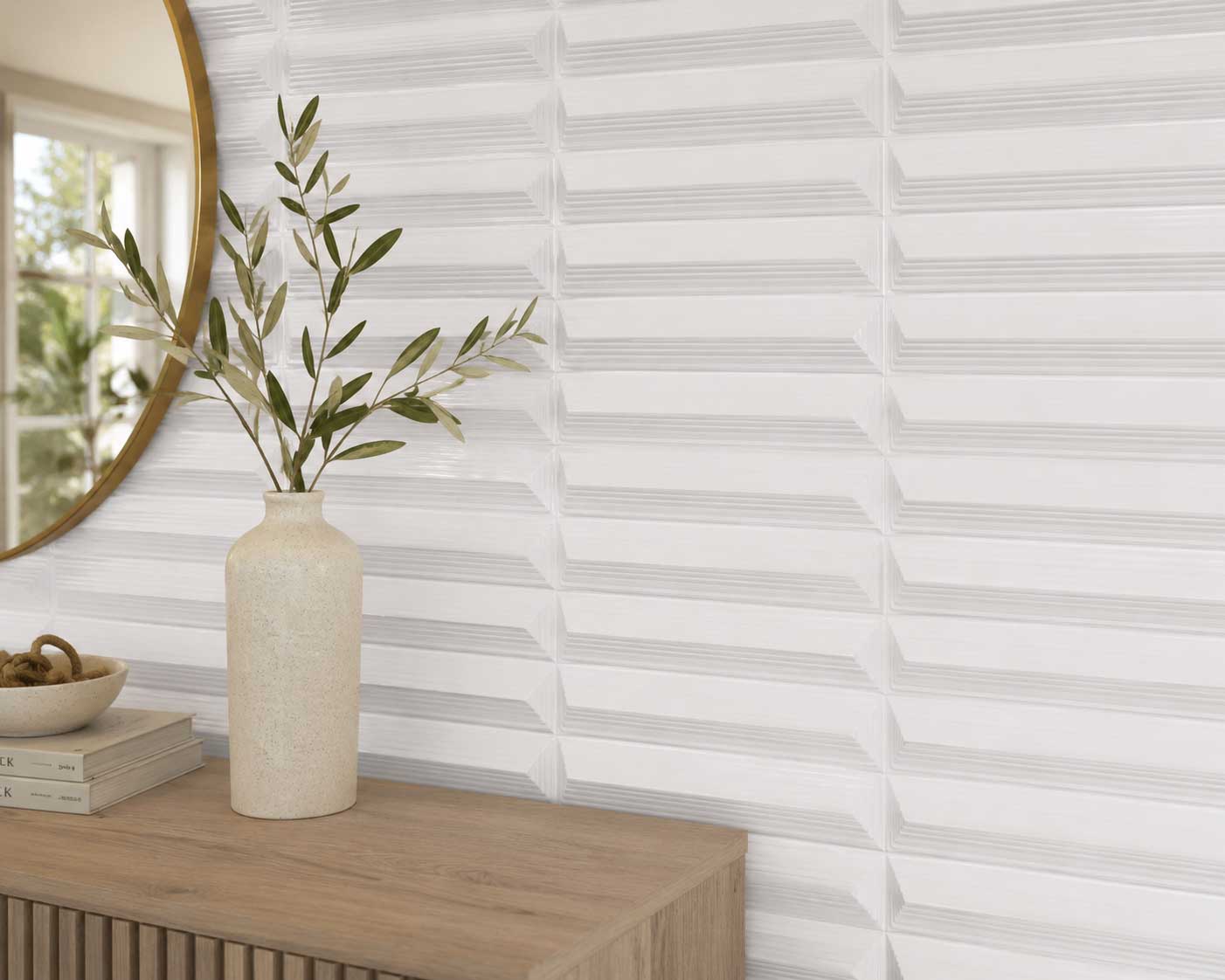 Close-up of a white ridged tile wall above a console with a vase and round mirror.