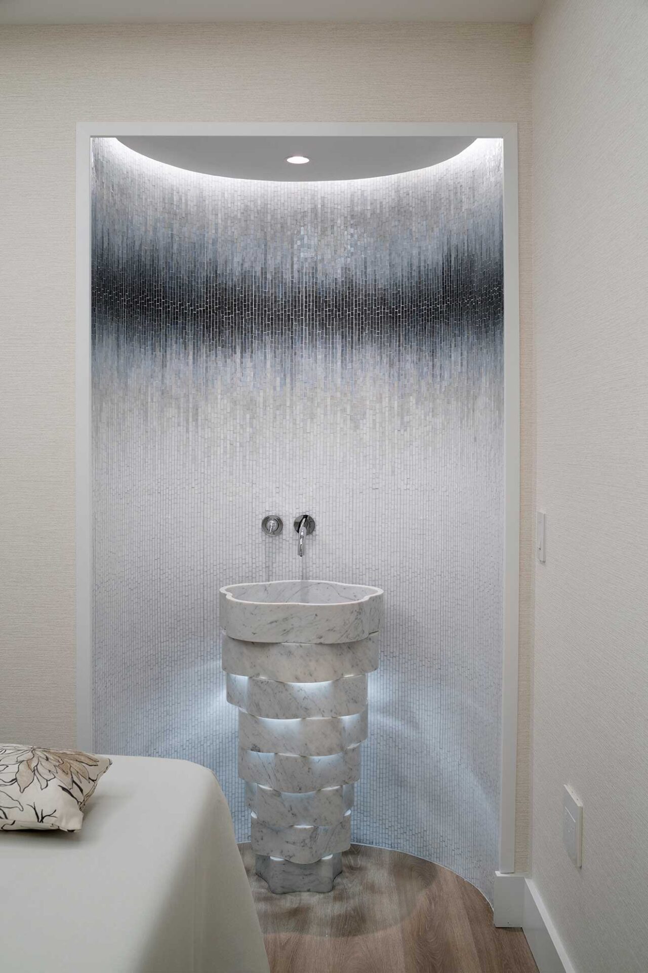 Round basin in an illuminated curved niche with a textured gray feature wall.
