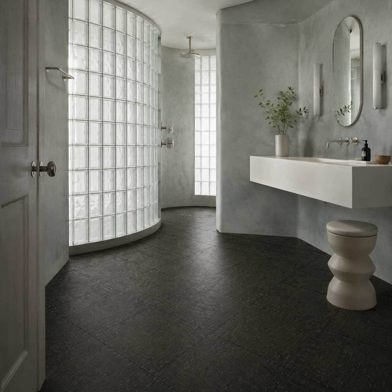 Bathroom with dark textured tile flooring, a curved glass-block shower and a floating vanity.