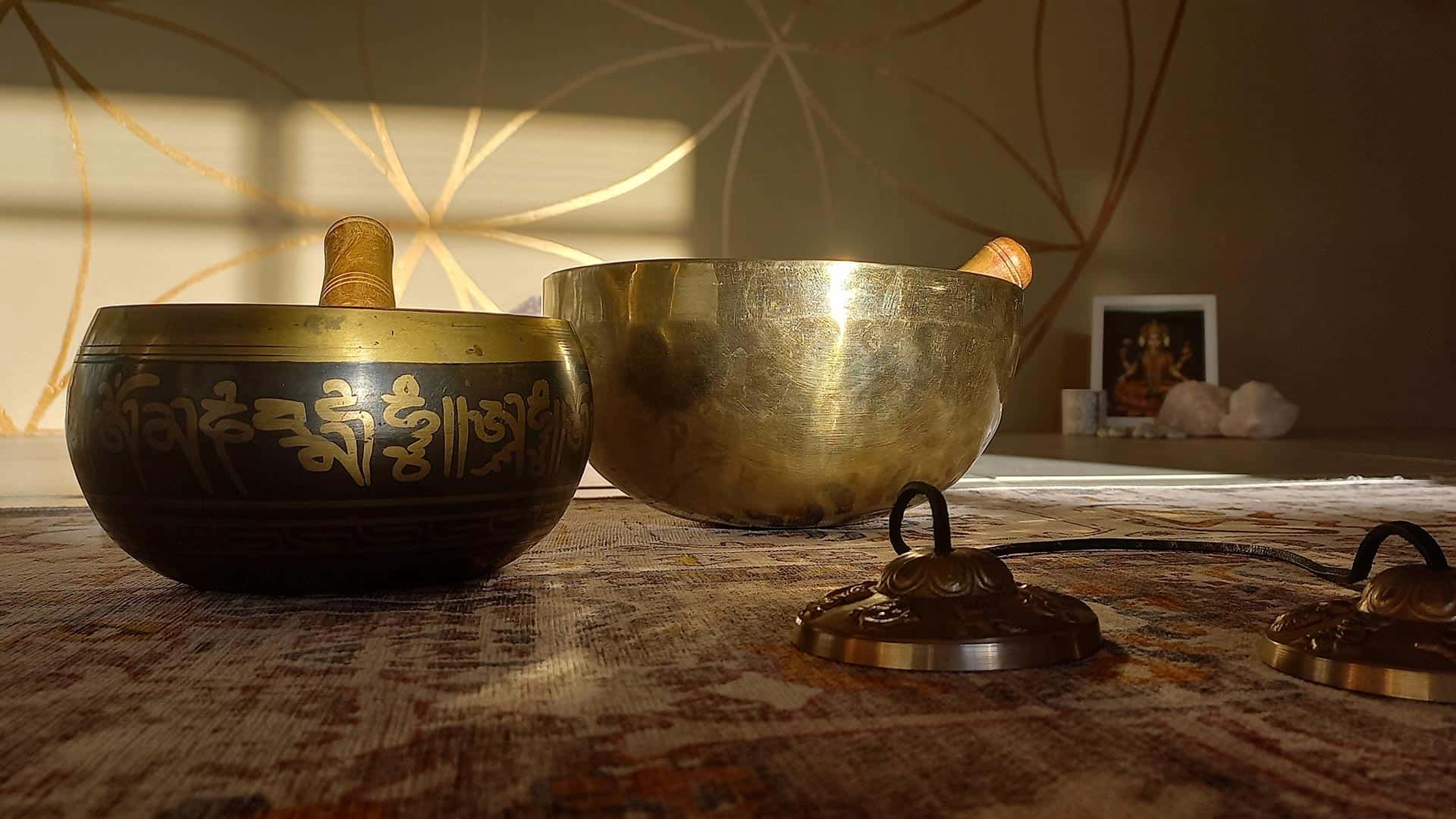 Two Tibetan singing bowls with a wooden mallet on a textured surface.