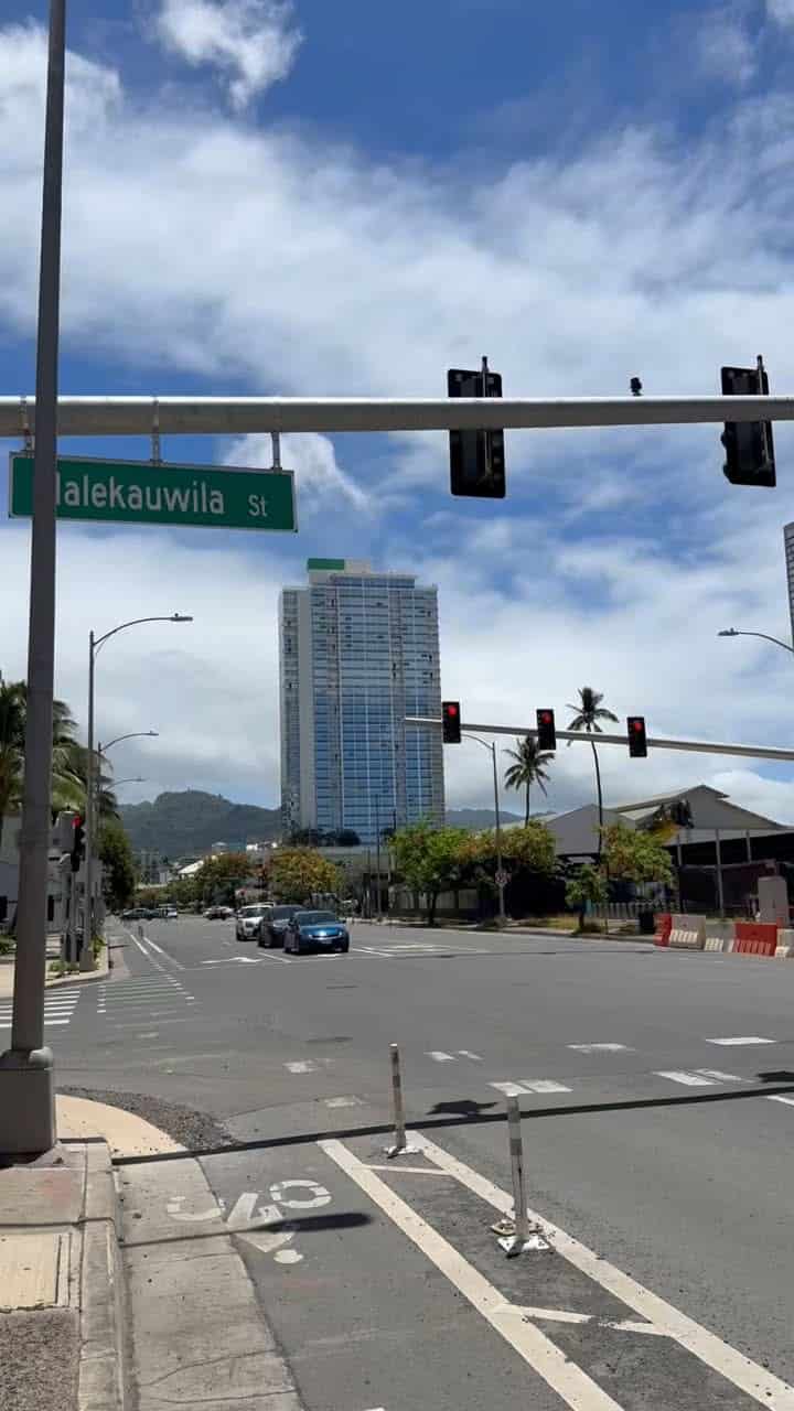 Street view in Honolulu showing traffic lights, a tall building, and a street sign for Kalakauwila Street, under a partly cloudy sky.