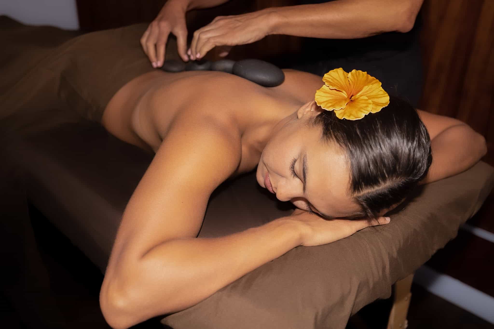 Relaxing massage in Honolulu with a woman receiving a back massage at a spa, featuring a tropical flower in her hair.