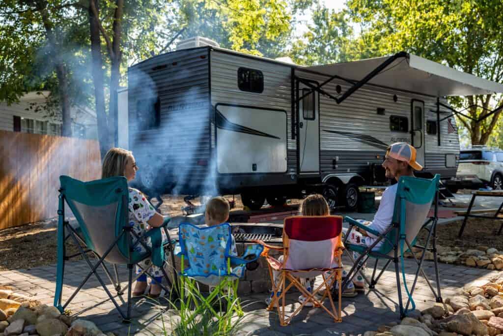 A family sits around a campfire in front of an rv.