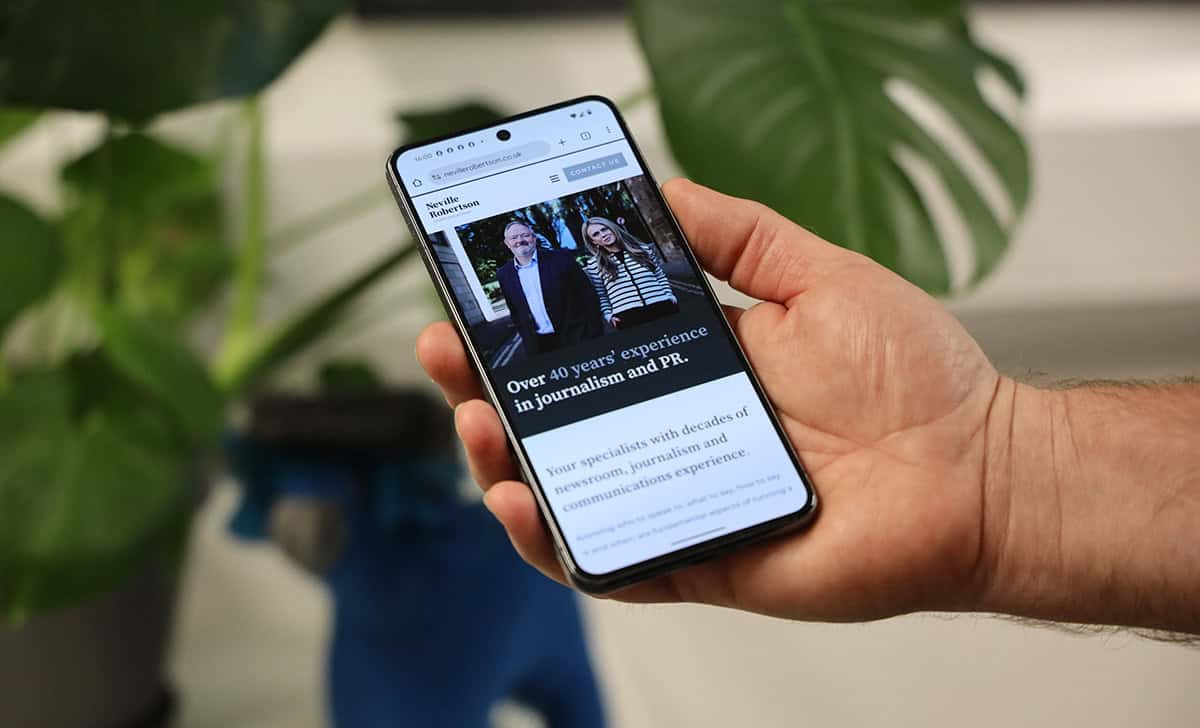 Person holding smartphone displaying a news article about journalism in Dundee.