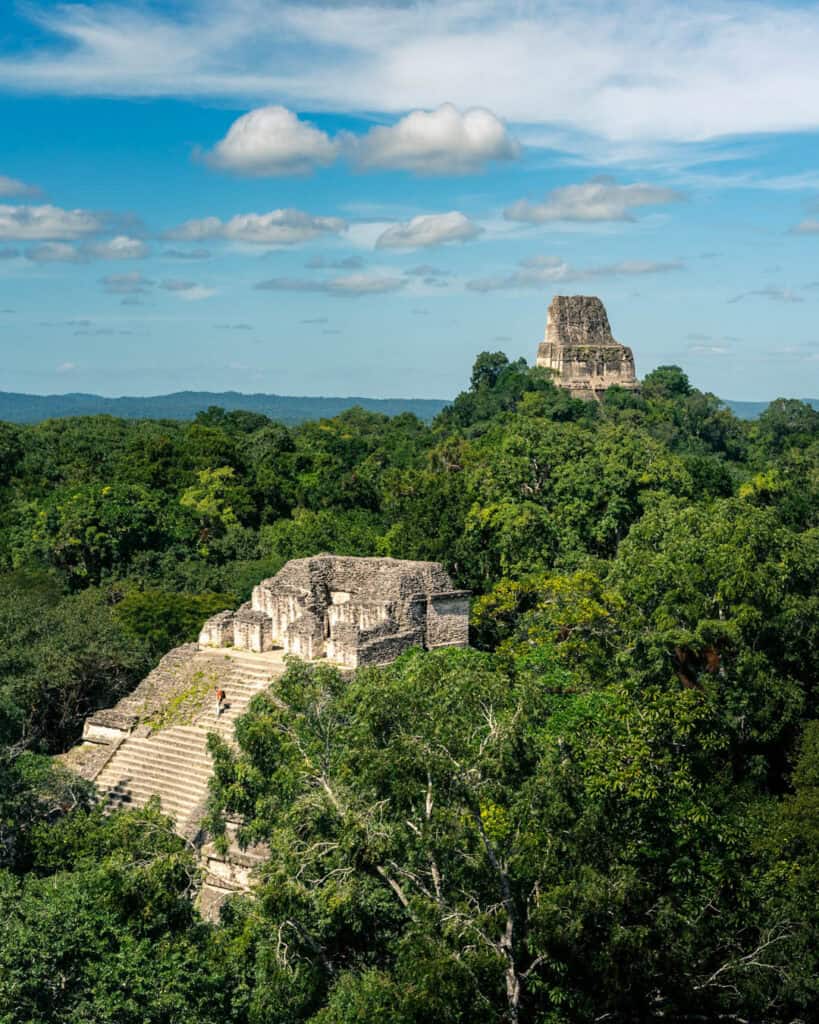 A single tourist climbing the steep stairs of the temples in Tikal national park, surrounded by the jungle and other temples