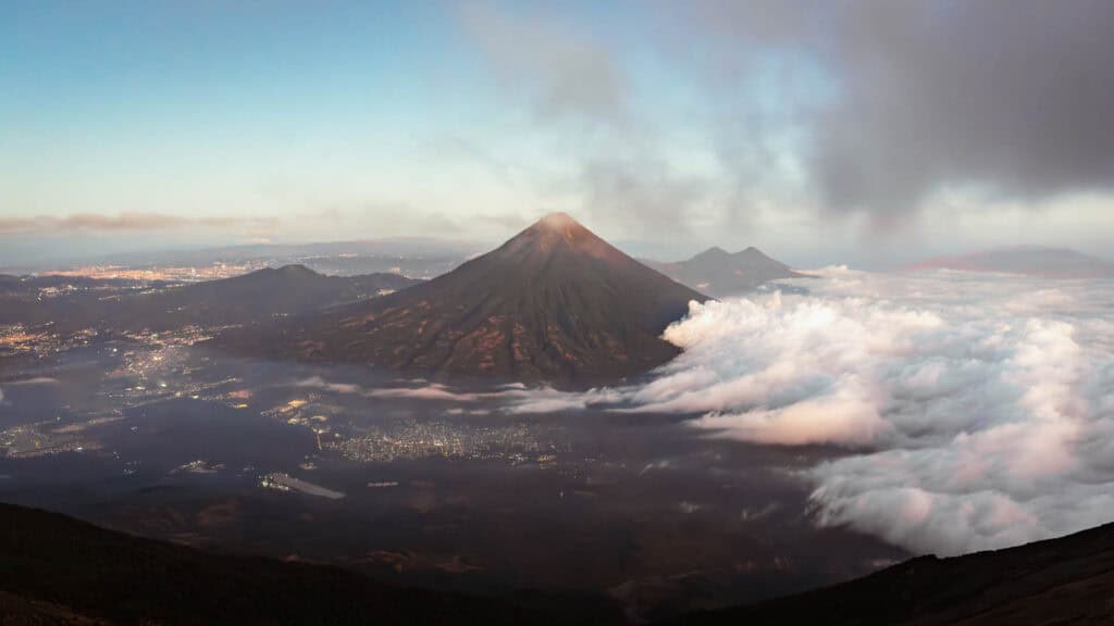 A wide shot of Antigua, rolling clouds and looming volcanoes in the background