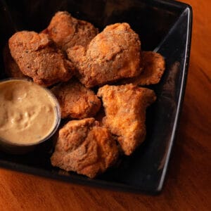 Crispy chicken bites with dipping sauce on a black plate.