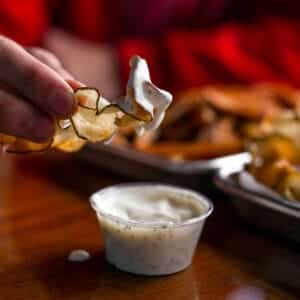 Hand dipping potato chip into creamy dipping sauce at Burger Rebellion.