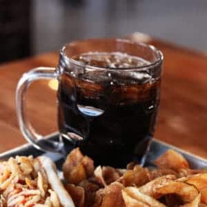 Refreshing dark soda served with crispy fried snacks on a wooden table.
