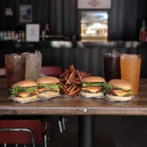 Four cheeseburgers with fries and drinks on a restaurant table.