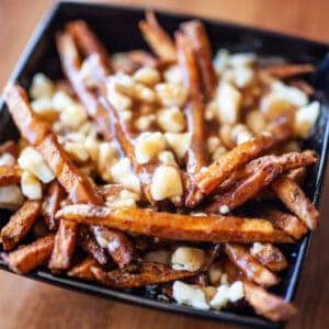 Close-up of poutine with fries, cheese curds, and gravy in a black bowl.