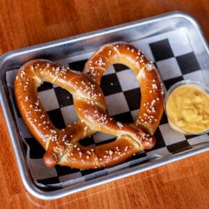 Freshly baked pretzel with coarse salt and mustard dip on a metal tray.