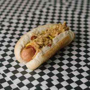 Hot dog with fried onions and mustard in a bun on checkered surface.