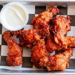 Crispy buffalo chicken wings with dipping sauce on checkered paper.