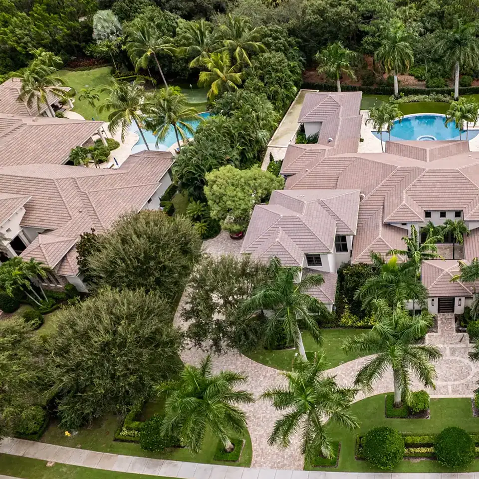 Elevated view of an Coastal Contemporary style exquisite home, encircled by flourishing palm trees and a pristine pool, showcasing a rich green oasis.