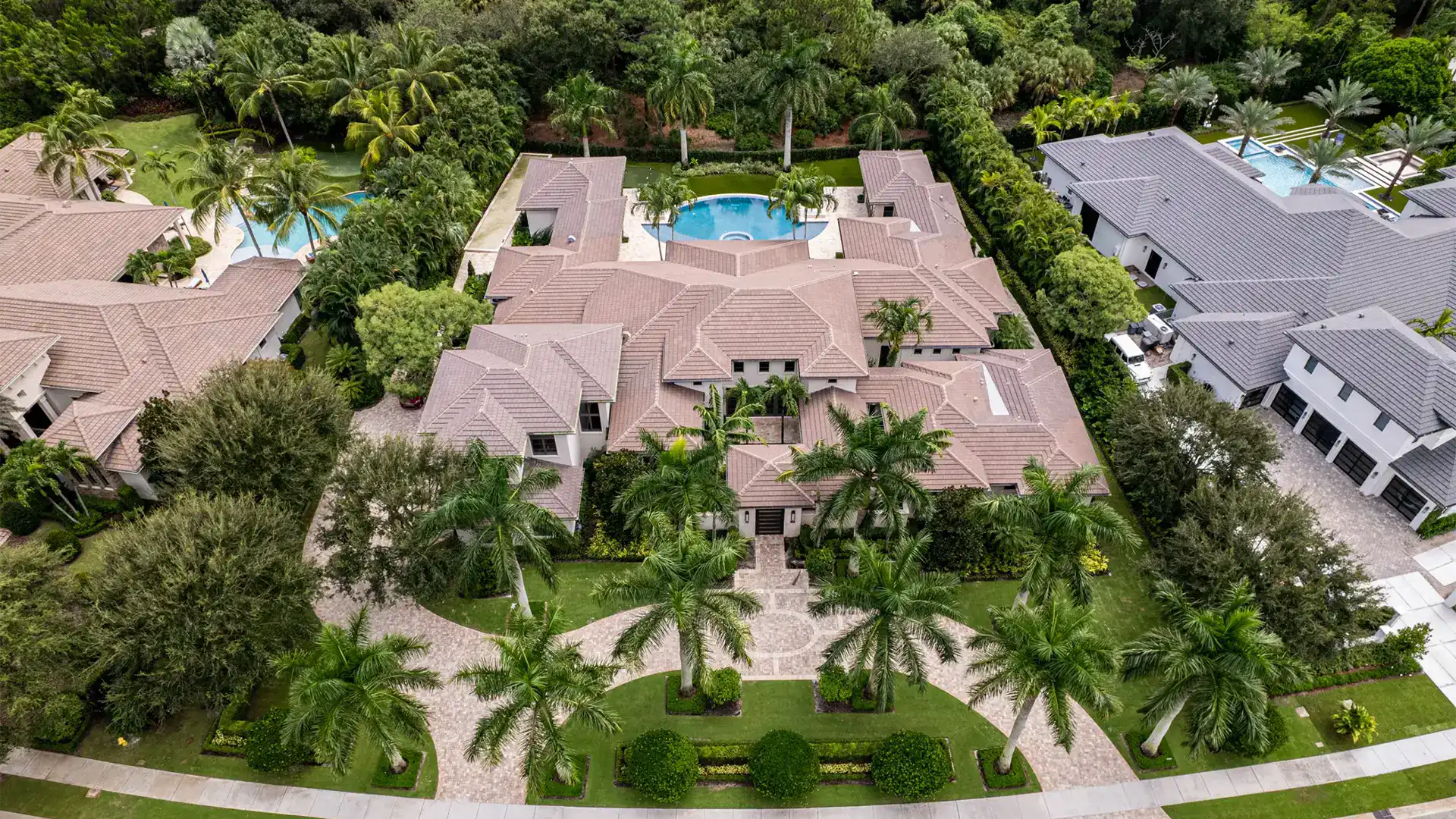 Elevated view of an Coastal Contemporary style exquisite home, encircled by flourishing palm trees and a pristine pool, showcasing a rich green oasis.