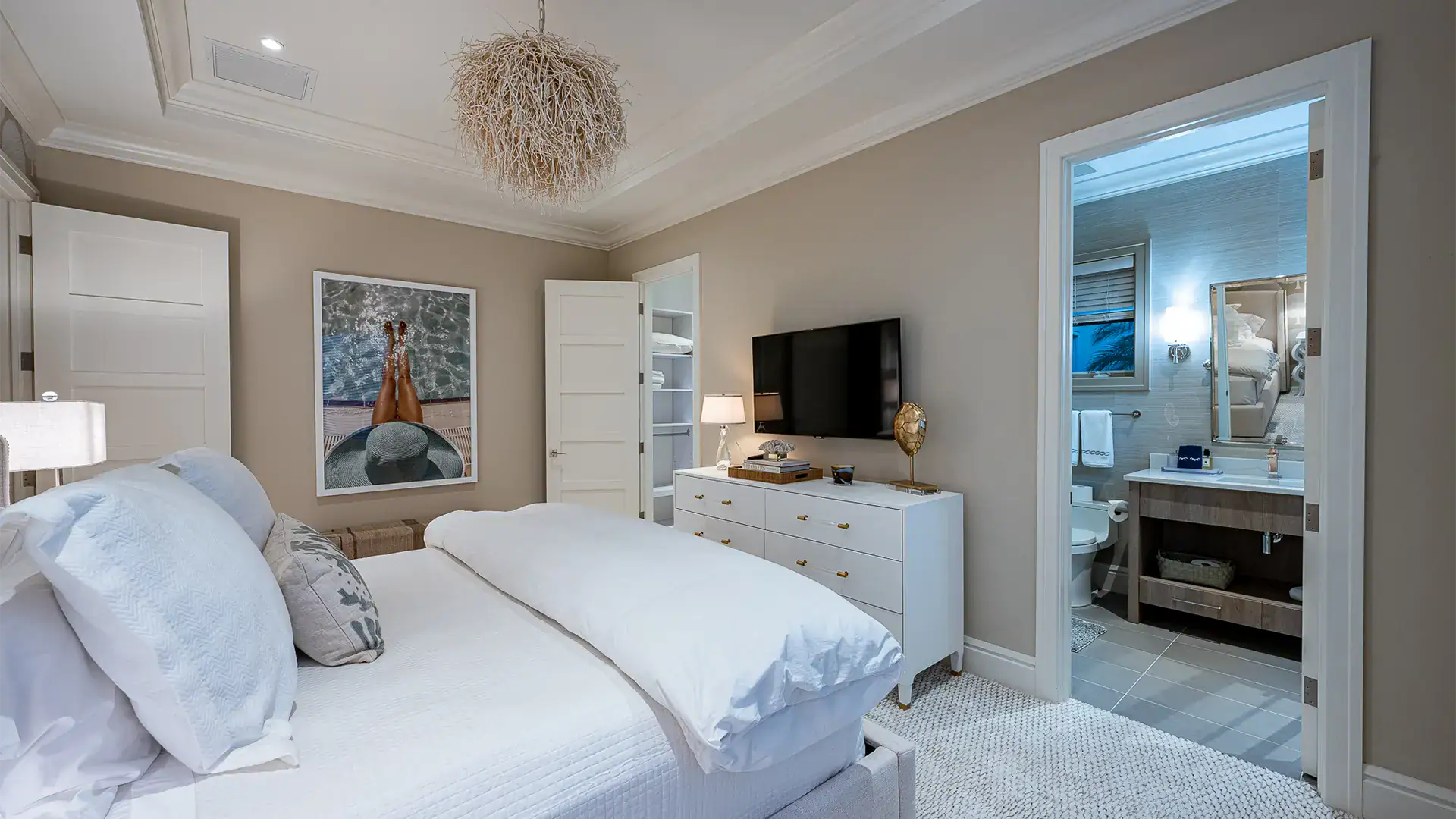 Refined bedroom enhanced by calming beige walls and a chic lamp, a white bed and television.