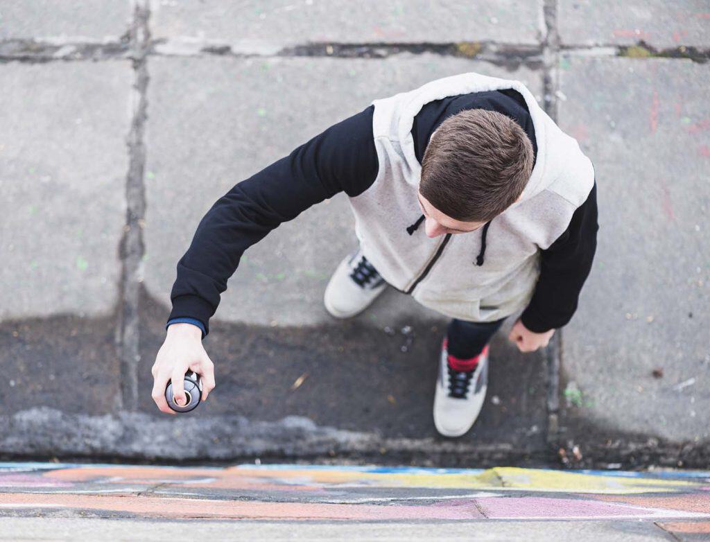 Young man spray painting graffiti on city wall, street art scene.