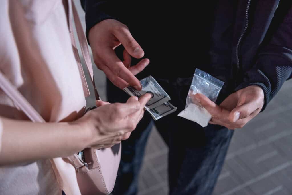 Drug deal exchange involving cash and small plastic bags in a public setting.