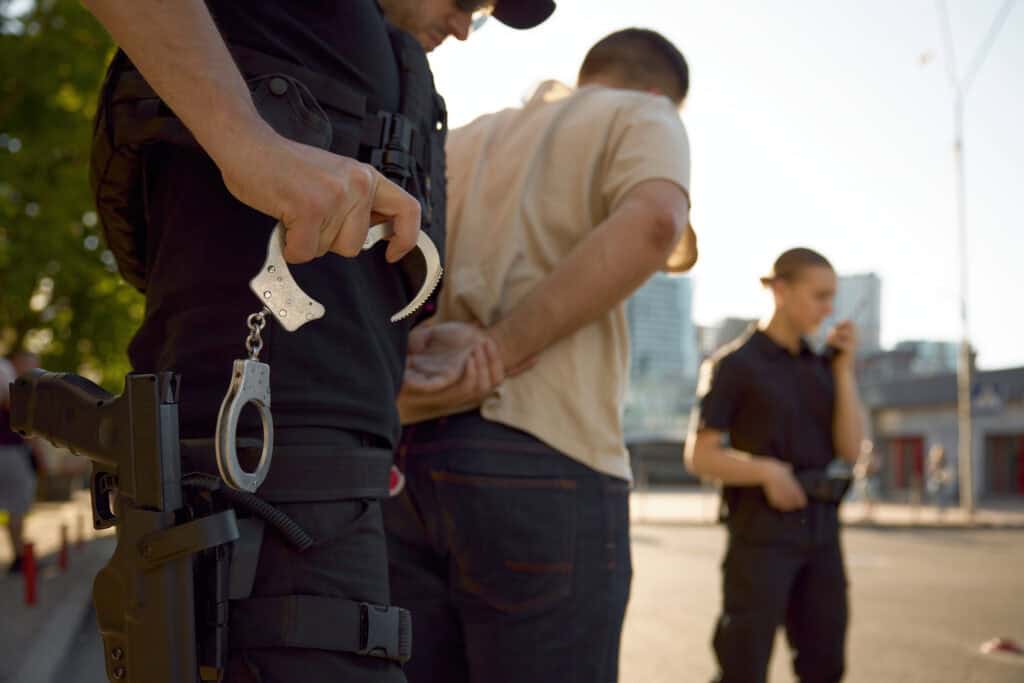 Man in police uniform arresting a suspect outdoors during daytime.