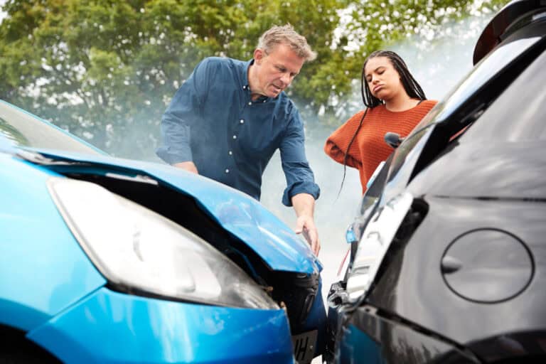 Accident scene with two people inspecting car damage after collision.