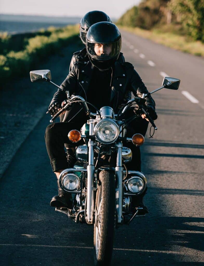 Motorcycle rider wearing a helmet and leather jacket riding on an open road.