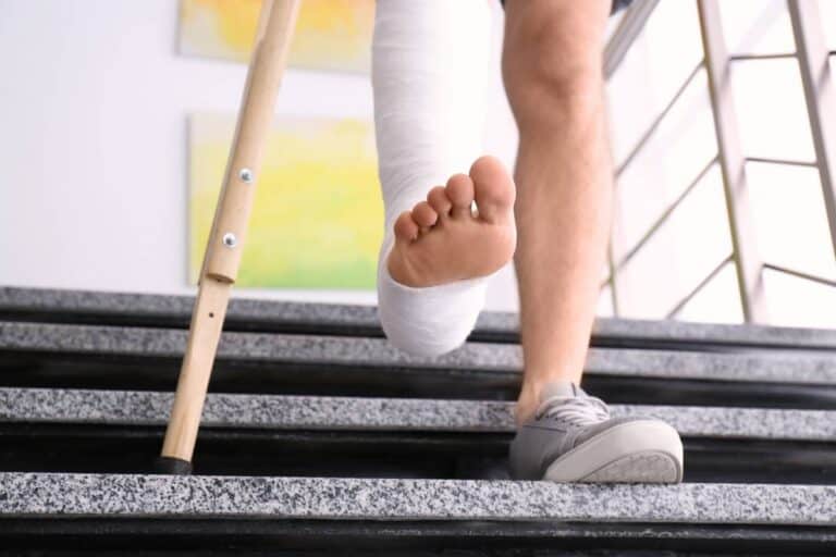 Person with injured leg in cast descending stairs, crutches nearby.