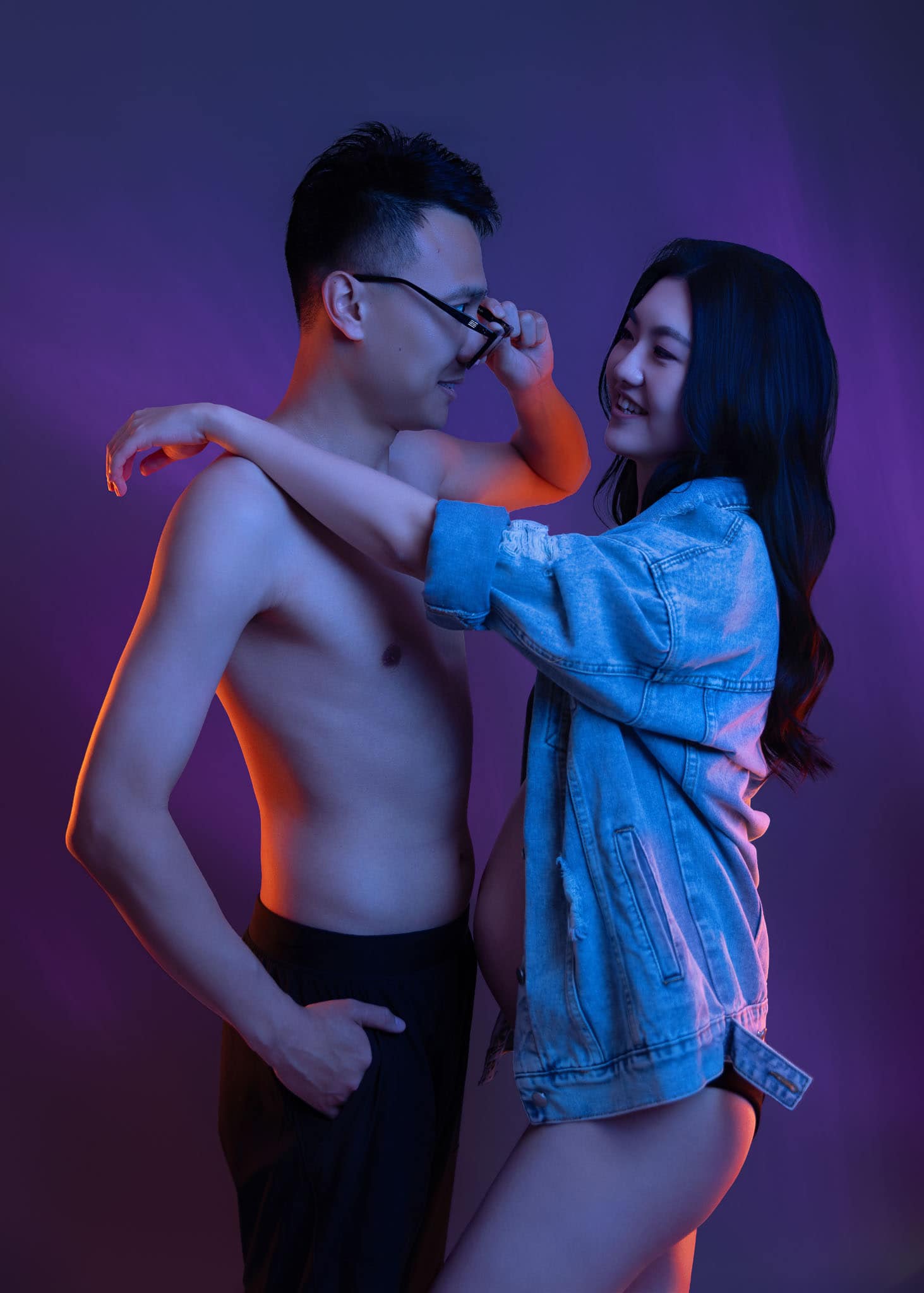 Young couple in playful pose with neon purple and blue lighting for their fashion maternity photo in Edmonton