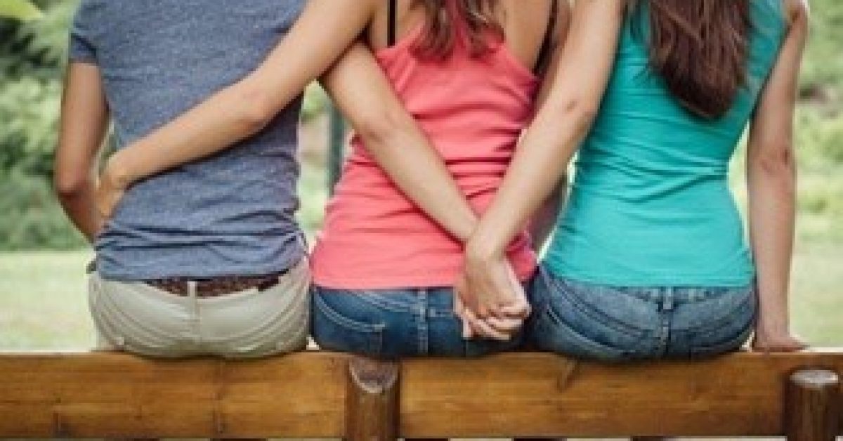 Love triangle, a girl is hugging a guy and he is holding hands with another girl, they are sitting together on a bench