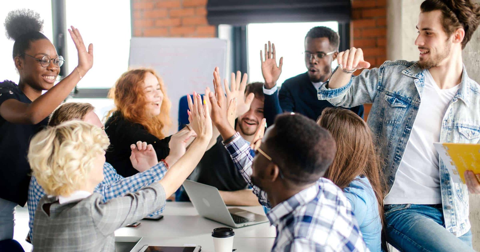 High-energy team meeting with diverse colleagues giving high fives and celebrating success in a modern office environment.