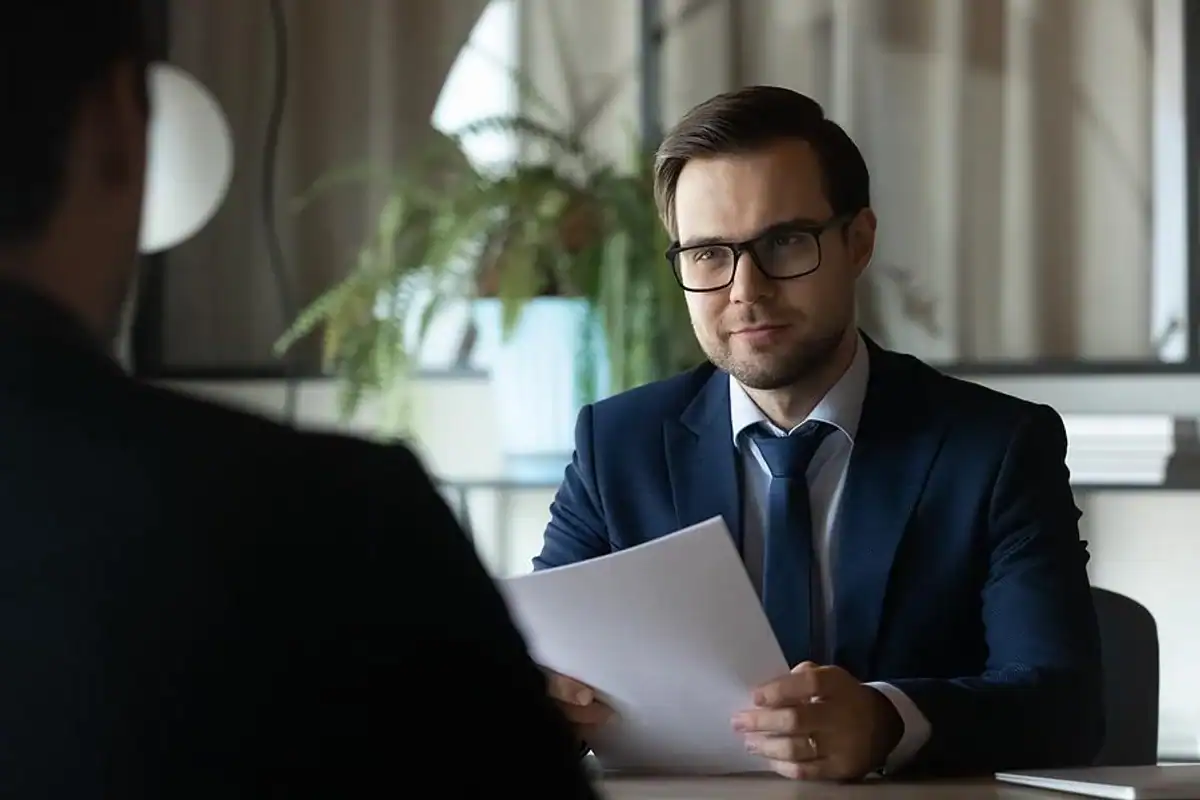 Elegant businessman in formal suit and glasses discussing documents during interview or meeting in modern office environment, emphasizing professionalism and corporate success.