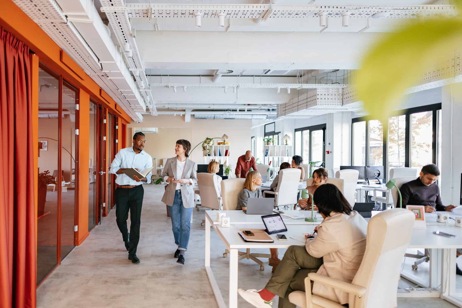 Modern coworking office space with diverse professionals working, collaborating, and networking in a bright, open-plan environment with large windows and contemporary furniture.