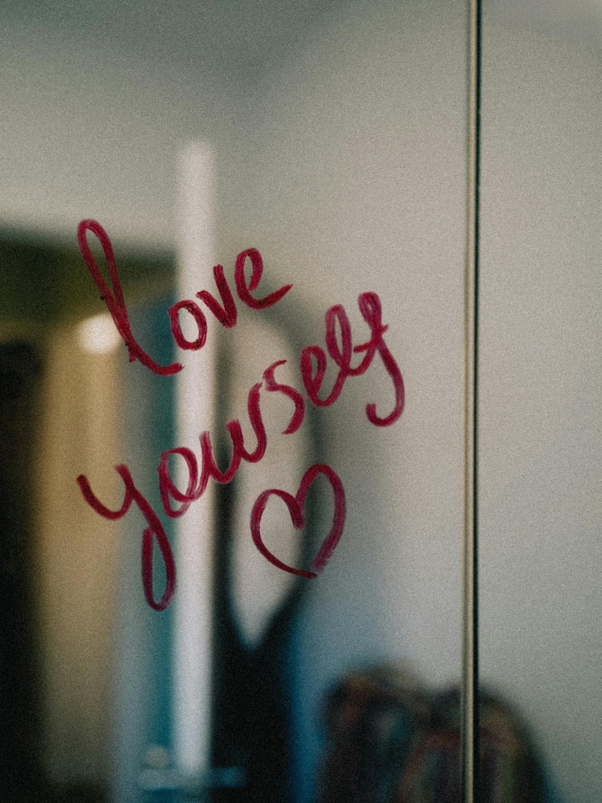 Positive affirmation written on a mirror in red lipstick: Love Yourself. Practical self-love exercises for trauma recovery