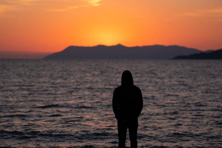 Person standing near the ocean horizon reflecting on trauma recovery and healing.
