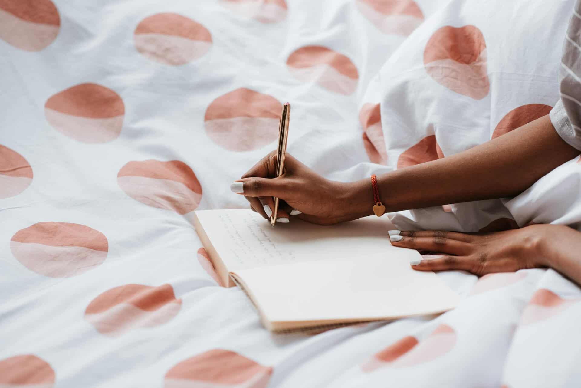 Woman writing in journal in bed — therapeutic journaling prompts for emotional healing and trauma recovery