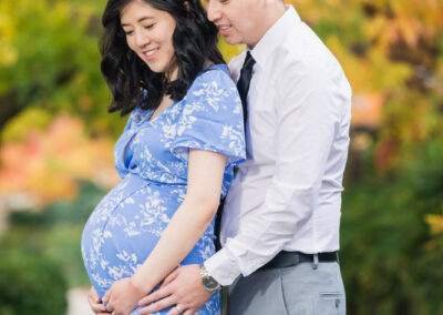 A pregnant couple in a blue dress is posing for a photo in the fall.