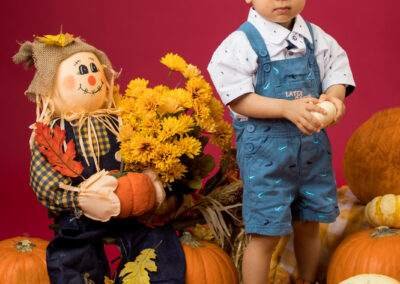 A boy is standing next to a scarecrow and pumpkins.